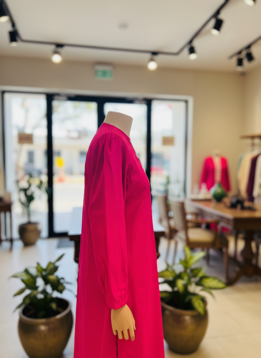 Mannequin wearing a bright pink dress with white lace details against a light curtain background