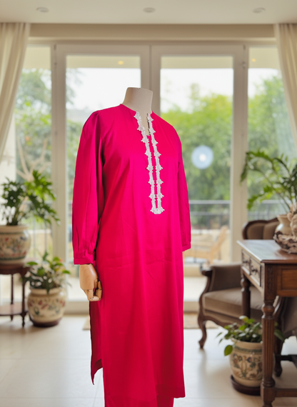 Mannequin wearing a bright pink dress with white lace details in a room with large windows and plants.