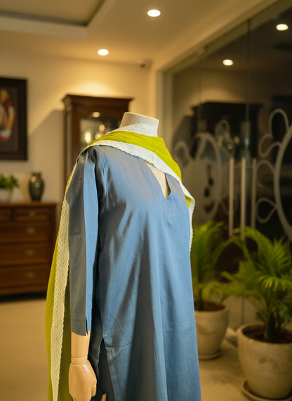 Mannequin wearing a blue outfit with green accents in a room with curtains.