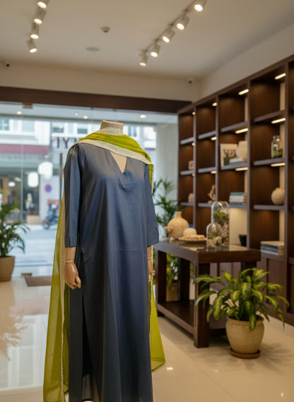 Mannequin wearing a blue garment with green accents against a light curtain background